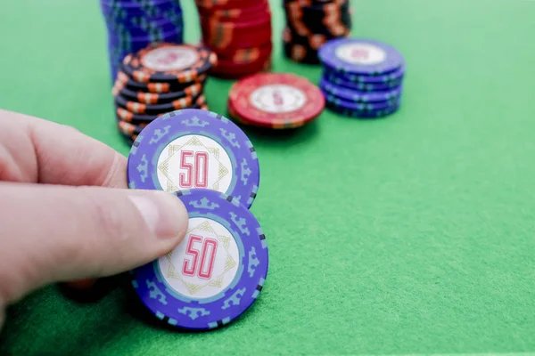Hand houden van twee blauwe poker chips naast een stapel chips — Stockfoto