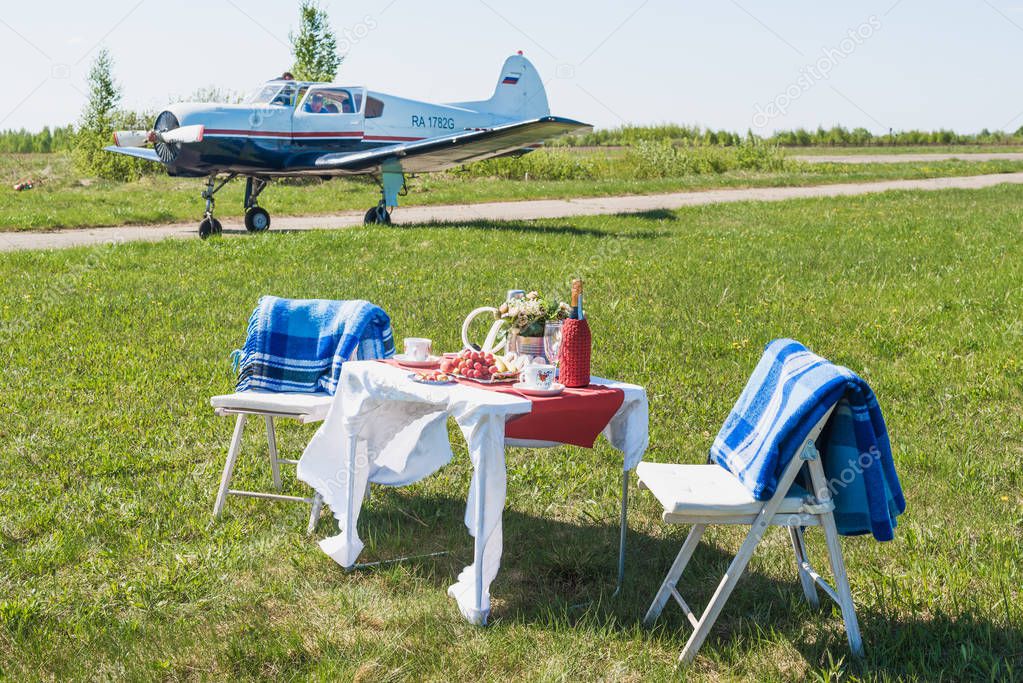 A table with fruits, sweets and wine for a date for two against a blue sky and with the plane that stands in the background