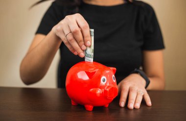 Latin bir kız bir masanın önüne oturur ve faturaları kırmızı bir kumbaraya koyar.