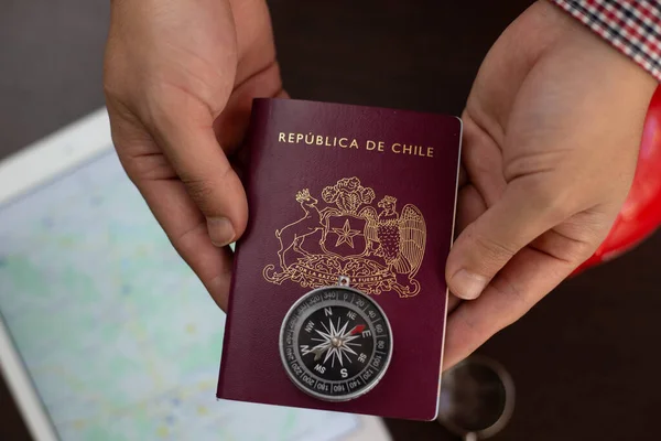 a person hands in front of a desk with a gray tablet and  a Chilean red passport  and a peggy bank and a magnifying glass