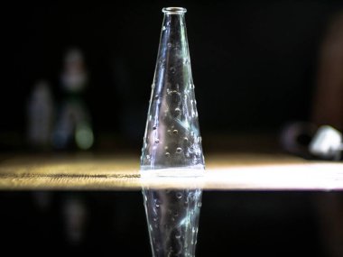 Siyah cam arka planda yansıyan cam şişe. Geceleri mutfakta çekilen vazonun ayrıntıları.