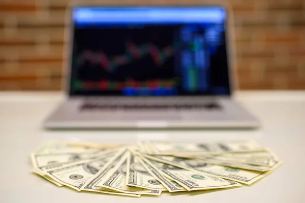 Dollar bills on a table with bitcoin charts laptop on background