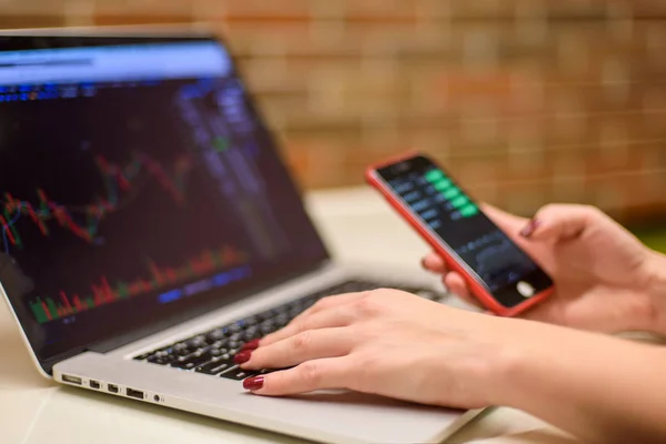 Dizüstü bilgisayar ve smartphone izlerken bitcoin grafikler ve hisse senetleri ile kız