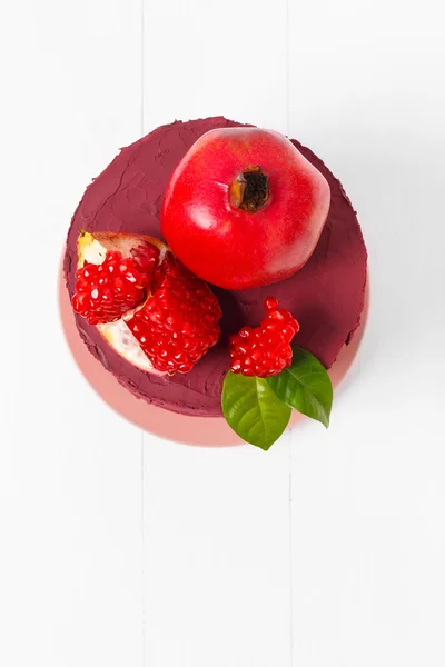 Top view of a sweet cake decorated with ripe pomegranate on a white wooden background — Stock Photo, Image
