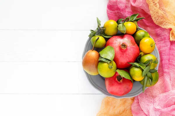 Un hermoso conjunto de frutas granada, mandarina, pera sobre textil rosa y fondo de madera blanco imagen horizontal Fotos De Stock Sin Royalties Gratis