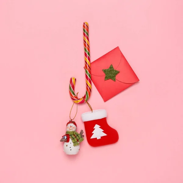 パステル ピンクの背景のキャンデー杖、雪だるま、クリスマス靴下、封筒の平面図です。新しい年の概念。シンプルなスタイルです。クリスマス装飾. — ストック写真