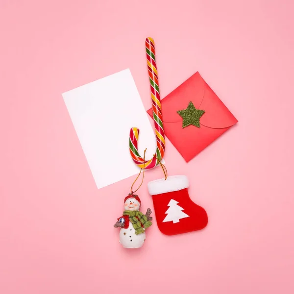 Boże Narodzenie makieta. Nowy rok pocztówka koncepcja. Widok z góry z trzciny cukrowej candy, bałwana, skarpety świąteczne wraz z kopertą na tle różowy pastel. — Zdjęcie stockowe
