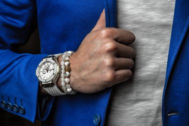 beyaz bilezik doğal taşlardan ve minerallerden yapılmış bir adamın elinde, beyaz bir saat ve mavi bir ceket