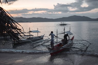 Filipinli balıkçılar, Filipinler 'in El Nido Palawan Adası' ndaki güzel bir günbatımında uzun bir balıkçılık gününden kalma geleneksel tekneleriyle bir körfeze dönüyorlar.