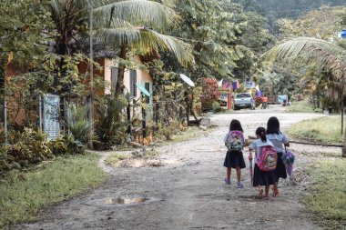 Filipinler 'in Barton Palawan Adası' ndaki çamurlu bir yolda okuldan eve dönen üç küçük Filipinli kız.