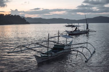 İki geleneksel Filipinli balıkçı, gün batımında Filipinler 'deki El Nido Palawan körfezine tekneleriyle dönüyorlar.