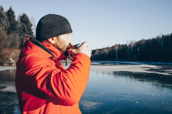 Ein einsamer Landstreicher steht auf Eis und trinkt Tee aus einer Thermoskanne. Stockfoto