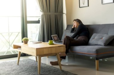 Asyalı Malezyalı kız kanepede tek başına oturmuş dizüstü bilgisayarla film izliyor.