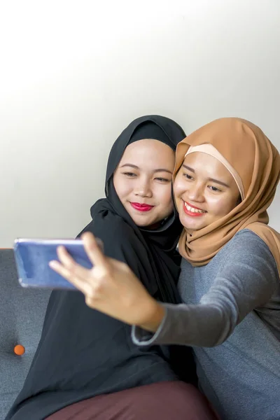 Dva malajští přátelé v hidžábu na pohovce — Stock fotografie