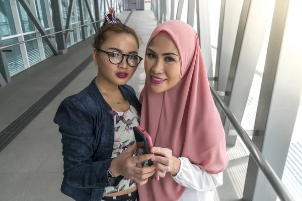 Two friends at the train station holding smartphone