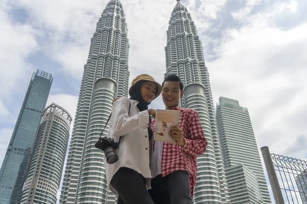 Turistický pár v Kuala Lumpur s úsměvem při pohledu na mapu diskutuje — Stock fotografie