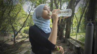 Malezyalı Müslüman kadın tesettürlü açık havada dinleniyor ve su içiyor