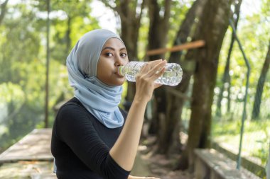 Malezyalı Müslüman kadın tesettürlü açık havada dinleniyor ve su içiyor