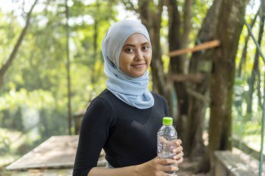 Malezyalı Müslüman kadın tesettürlü açık havada dinleniyor ve su içiyor