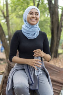 Malezyalı Müslüman kadın tesettürlü açık havada dinleniyor ve su içiyor