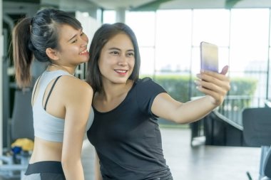 Sağlıklı Kavram, spor salonundaki tatlı Asyalı kız akıllı telefon kullanarak selfie çekiyor.