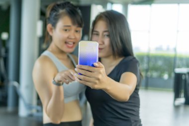 Sağlıklı konsept, spor salonunda telefona odaklanmış akıllı telefonu kullanan tatlı Asyalı kız.