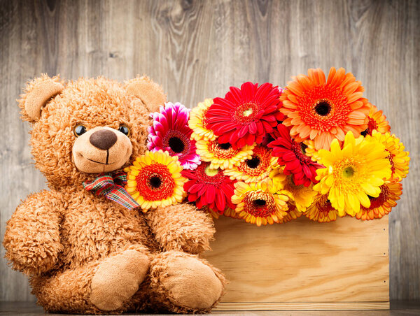 Flowers and a teddy bear on wooden background