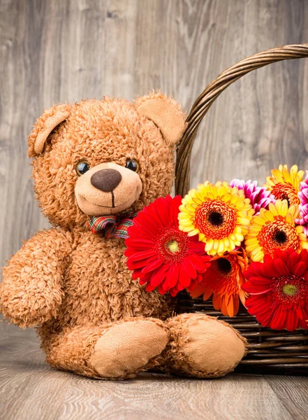 Beautiful flowers in the basket and a teddy bear on wooden background — Stock Photo, Image