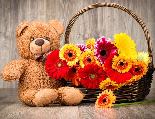 Hermosas flores en la cesta y un oso de peluche sobre fondo de madera —  Fotos de Stock