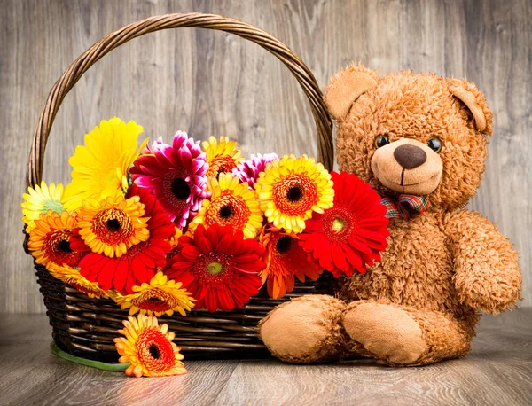 Beautiful flowers in the basket and a teddy bear on woooden background — Stock Photo, Image