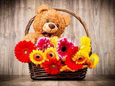 Sepet ve bir oyuncak ayı ahşap zemin üzerine güzel çiçekler