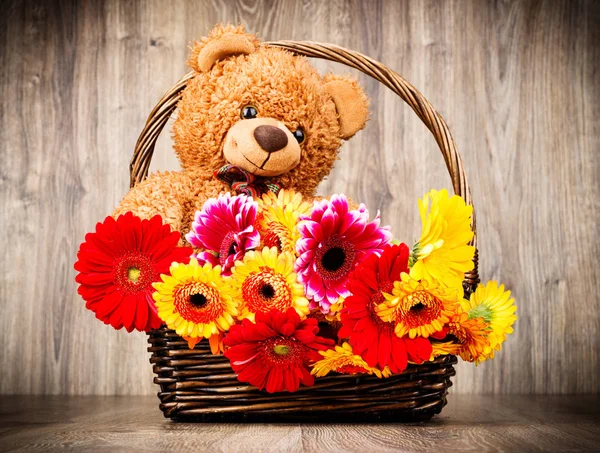 Hermosas flores en la cesta y un oso de peluche sobre fondo de madera — Foto de Stock