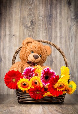 Sepet ve bir oyuncak ayı ahşap zemin üzerine güzel çiçekler