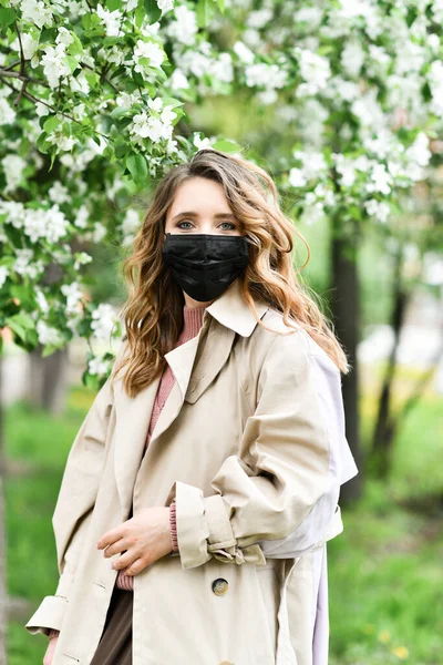 Arka planda maske takmış elma ağacı açan bir kız. Kavram ve sembol COVID-19 ve pandemik koronavirüsü karantinaya alır. 2020 baharında çiçek açan bahçede virüse ve alerjiye karşı koruma
