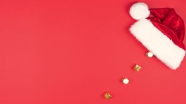 Yılbaşı balolarının, hediyelerin ve Noel Baba şapkalarının hareketli animasyonlarını durdurun. Noel topları ve kırmızı şapkayla yatıyordu. Üst Manzara. Tatil kavramı, satış. Boşluğu kopyala