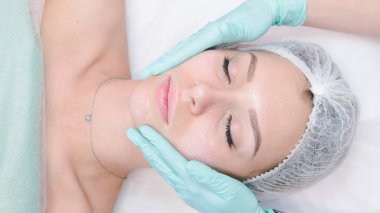 Kadın dermatolog, güzel bir kızın yüzüne masaj yapıyor.