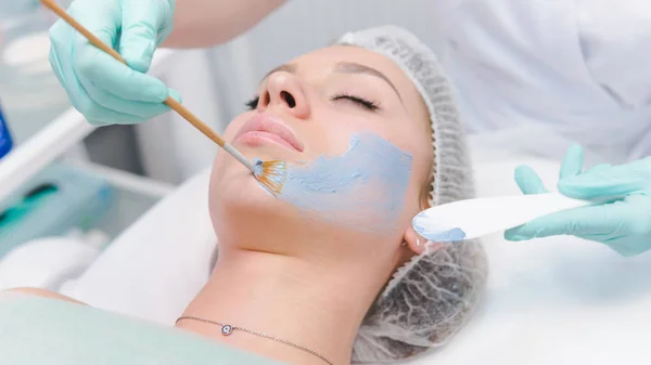La cosmetóloga femenina que aplica la máscara de cosmetología azul a los jóvenes — Foto de Stock