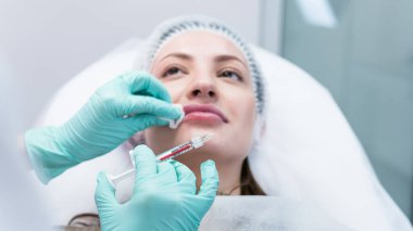 Genç güzellik uzmanı kadın dudaklarına iğne yapmaya hazırlanıyor. Doktor kozmetik uzmanı dudak büyütme prosedürü uyguluyor. Güzellik salonu ve estetik cerrahi kliniği kavramı.