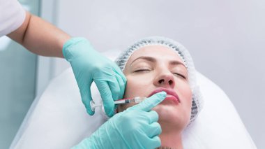 Genç güzellik uzmanı kadın dudaklarına iğne yapmaya hazırlanıyor. Doktor kozmetik uzmanı dudak büyütme prosedürü uyguluyor. Güzellik salonu ve estetik cerrahi kliniği kavramı.