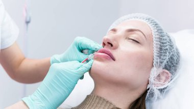 Genç güzellik uzmanı kadın dudaklarına iğne yapmaya hazırlanıyor. Doktor kozmetik uzmanı dudak büyütme prosedürü uyguluyor. Güzellik salonu ve estetik cerrahi kliniği kavramı.