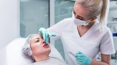 Genç güzellik uzmanı kadın dudaklarına iğne yapmaya hazırlanıyor. Doktor kozmetik uzmanı dudak büyütme prosedürü uyguluyor. Güzellik salonu ve estetik cerrahi kliniği kavramı.
