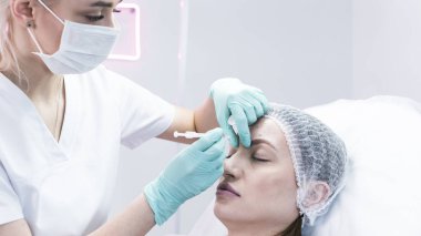 Genç güzellik uzmanı kadın alnına iğne yapmaya hazırlanıyor. Doktor kozmetik uzmanı yaşlanmayı önleme ve yüz gerdirme ameliyatı yapıyor. Güzellik salonu ve estetik cerrahi kliniği kavramı.