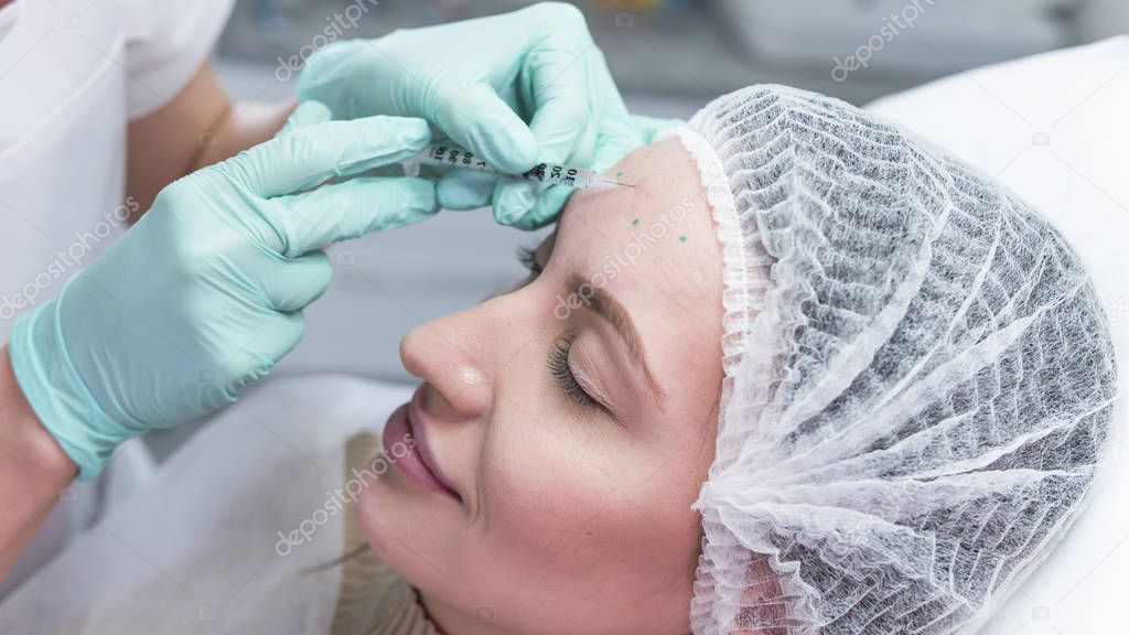 The young beautician doctor preparing to making injection in female forehead. The doctor cosmetologist makes anti-aging treatment and face lift procedure. Concept of beauty salon and plastic surgery clinic.