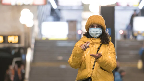 The young europeans woman in protective disposable medical face mask using antiseptic in the subway. New coronavirus (COVID-19). Concept of health care during an epidemic or pandemic