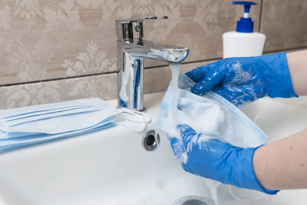 Close-up of female hands washing disposable medical face mask with soap. Deficiency of personal care product during the epidemic or pandemic. Concept of health care