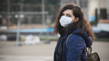 Yakın plan bir portre. Koruyucu, tek kullanımlık tıbbi maske takan genç Avrupalı bir kadın. Yeni koronavirüs (Covid-19). Salgın veya salgın sırasında sağlık hizmeti kavramı