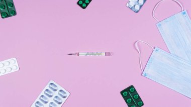 Koruyucu ilaç maskesi, antiseptik termometre ve pembe arka planda haplar. Doktor masası ve sağlık hizmeti kavramı. Üst görünüm, alanı kopyala