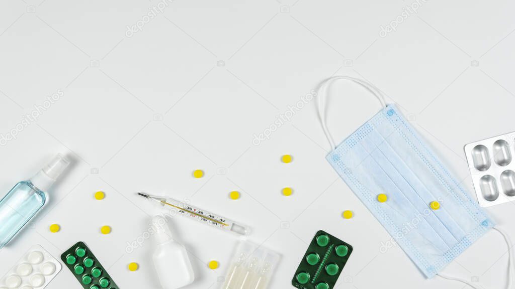 Protective medicine mask, antiseptic, thermometer and pills, flat lay. Concept of doctor table and health care. Top view, copy space