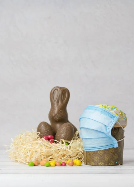 Easter cake in protective medical face mask and chocolate eggs and rabbit, close-up. Protection against viruses. The concept of the celebration of Holy Easter 2020 during coronavirus pandemic