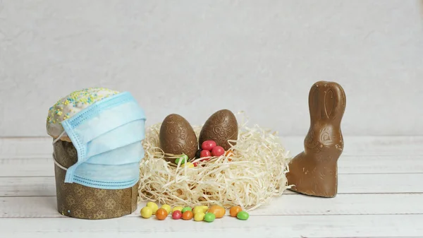 Easter cake in protective medical face mask and chocolate eggs and rabbit, close-up. Protection against viruses. The concept of the celebration of Holy Easter 2020 during coronavirus pandemic